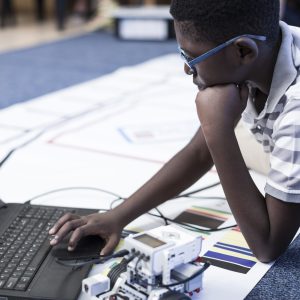 schoolboy with laptop in robotics class testing vehicle on test track